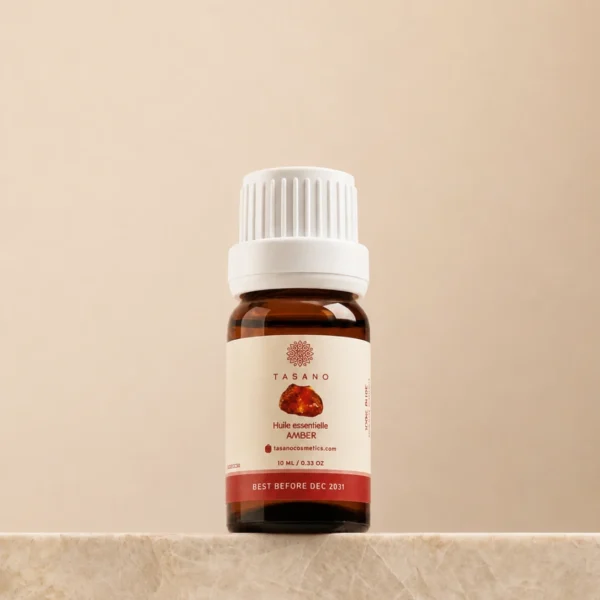 TASANO Amber Essential Oil 10 ml bottle on beige marble pedestal, Moroccan aromatherapy oil in premium amber glass packaging.