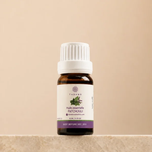 TASANO Patchouli Essential Oil 10 ml bottle on beige marble pedestal, Moroccan aromatherapy oil in amber glass.