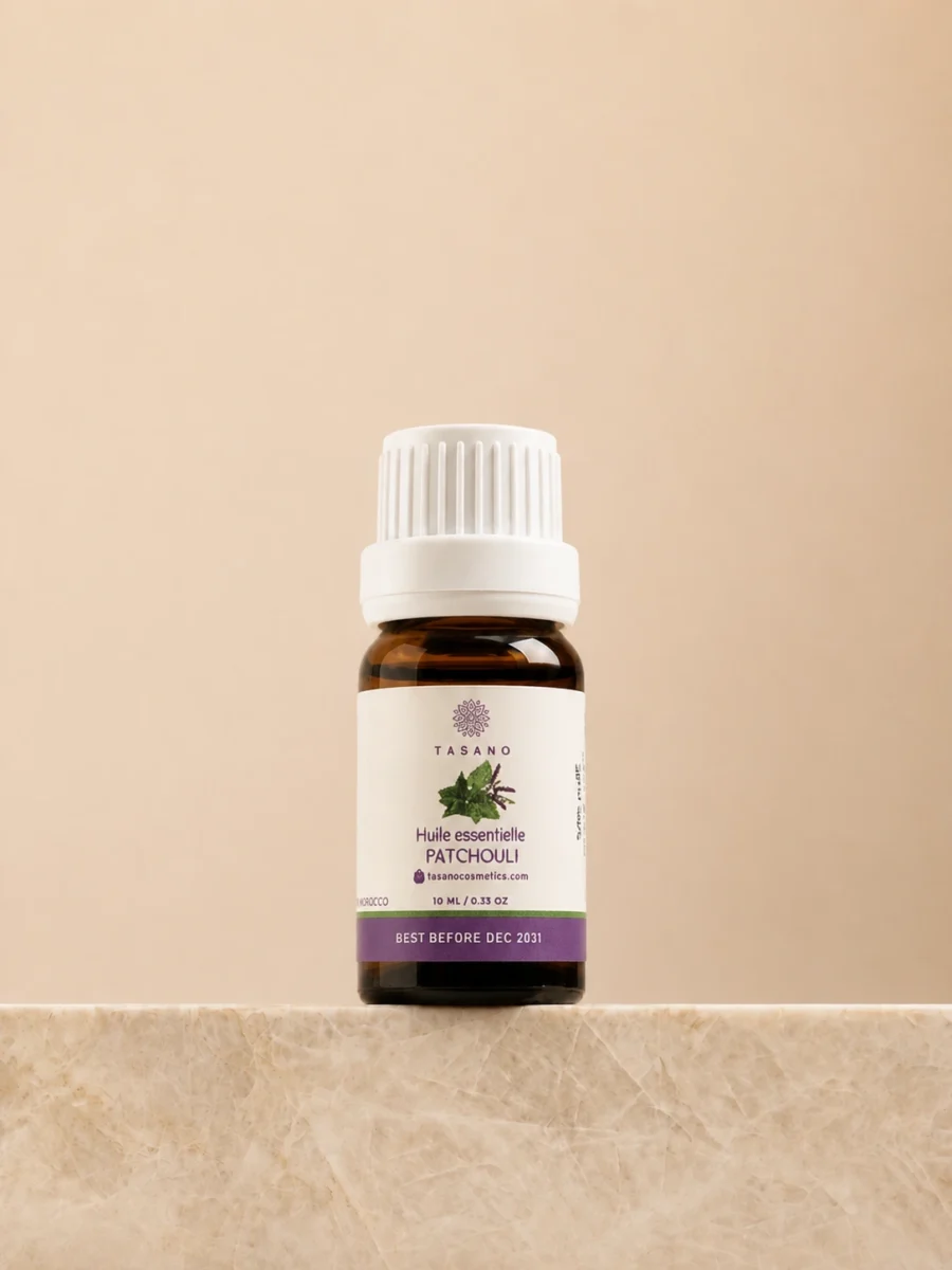TASANO Patchouli Essential Oil 10 ml bottle on beige marble pedestal, Moroccan aromatherapy oil in amber glass.