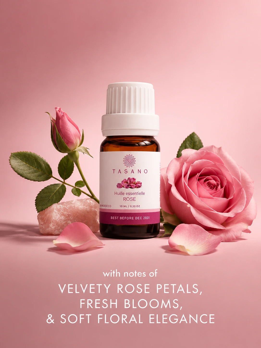 TASANO Rose essential oil bottle surrounded by rose petals and floral elements on a rose-toned background showing its delicate romantic scent profile.