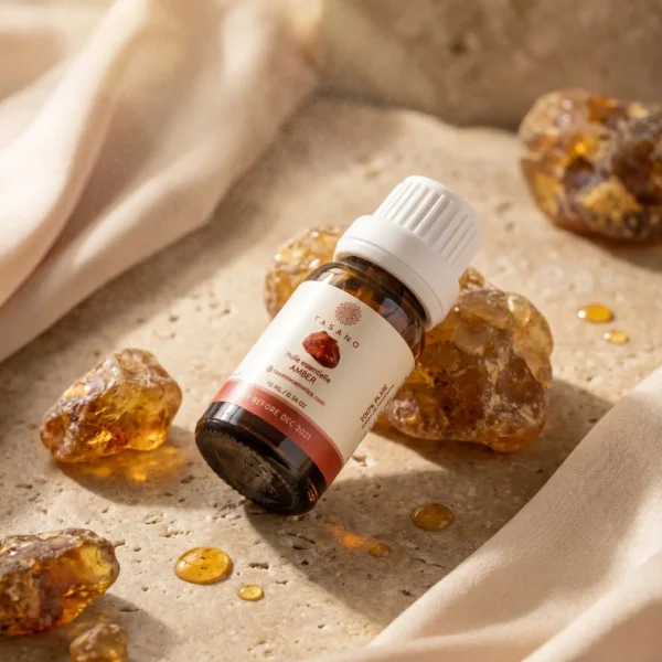 TASANO Amber Essential Oil styled with raw amber resin, warm oil drops, silk fabric, and natural sunlight on beige stone.