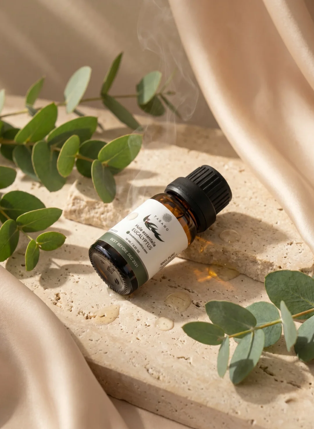 TASANO Eucalyptus Essential Oil styled with fresh eucalyptus leaves, pale oil drops, silk texture, and natural sunlight.