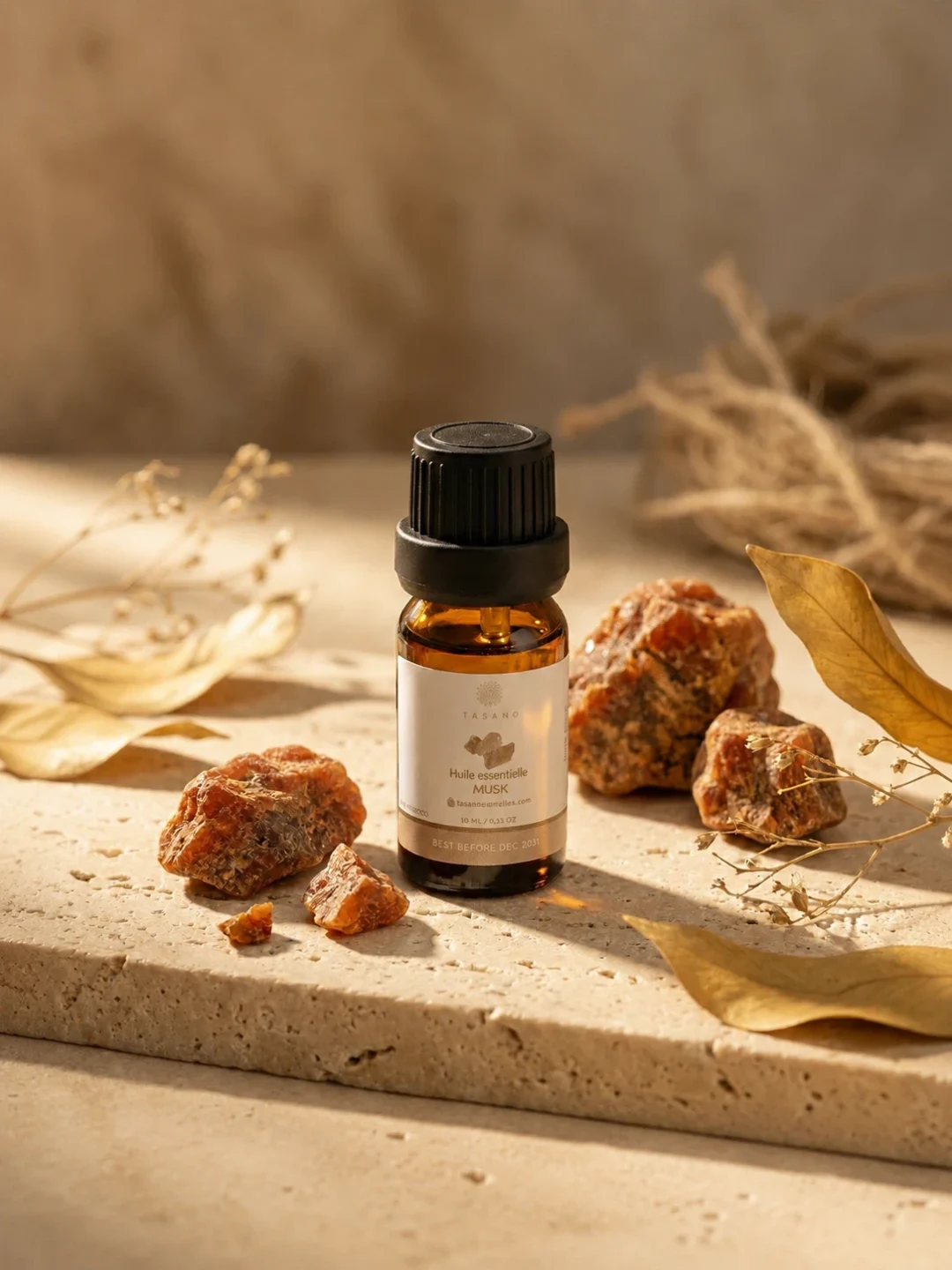 TASANO Musk Essential Oil styled with raw musk stones, deep amber oil drops, silk fabric, and warm sunlight.