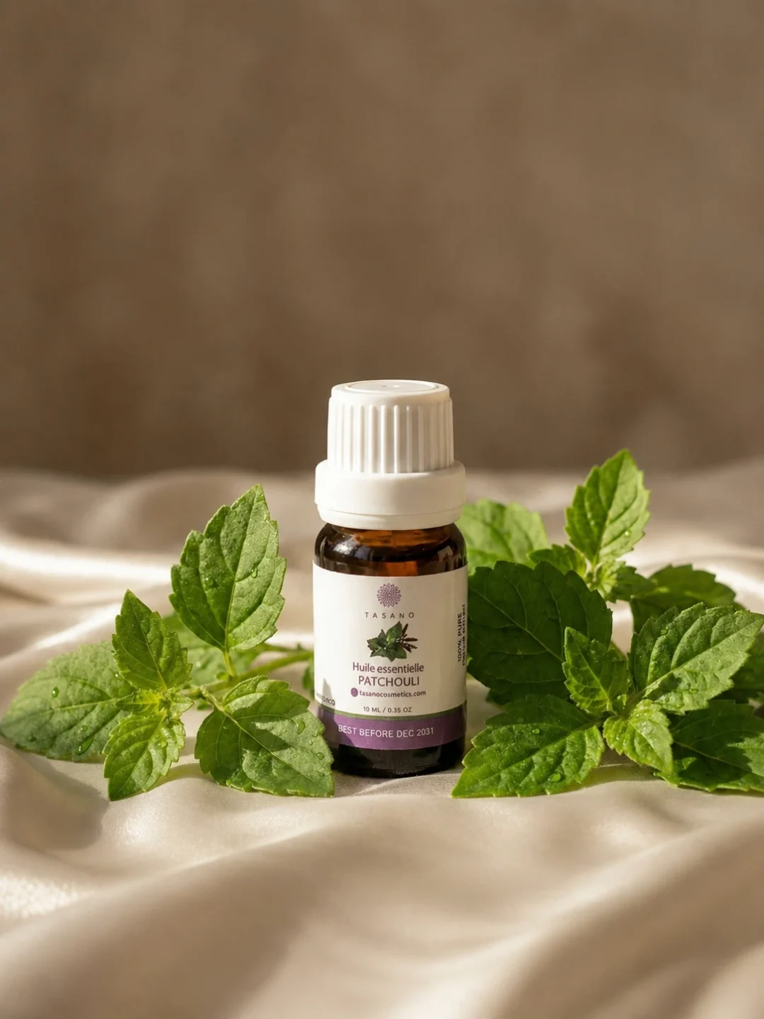 TASANO Patchouli Essential Oil styled with fresh patchouli leaves, silk surface, natural sunlight, and beige textures.