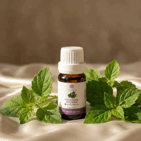 TASANO Patchouli Essential Oil styled with fresh patchouli leaves, silk surface, natural sunlight, and beige textures.