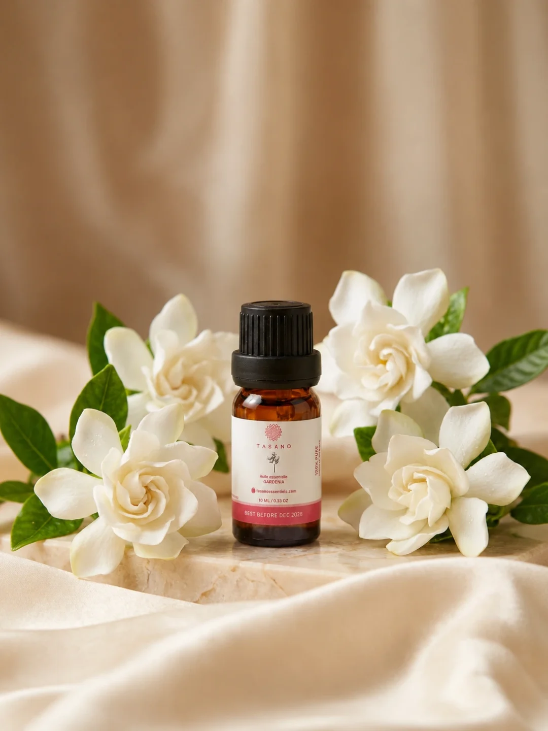 TASANO Gardenia Essential Oil styled with fresh gardenia flowers, pale yellow oil drops, silk fabric, and beige stone.