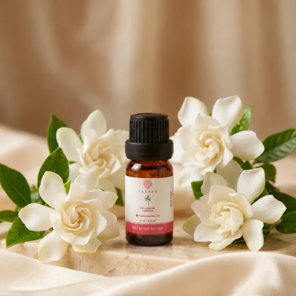TASANO Gardenia Essential Oil styled with fresh gardenia flowers, pale yellow oil drops, silk fabric, and beige stone.