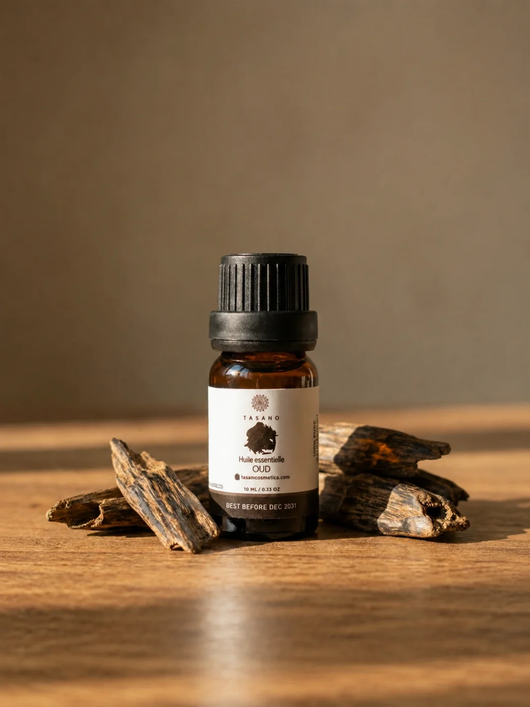 TASANO Oud Essential Oil styled with oud wood chips, rich amber oil drops, warm sunlight, and beige stone texture.